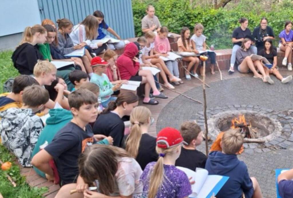 Kinder sitzen mit Büchern am Lagerfeuer